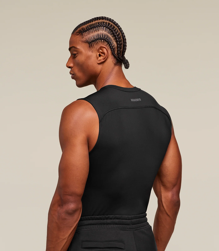 Person wearing a black sleeveless top and pants on a beige background