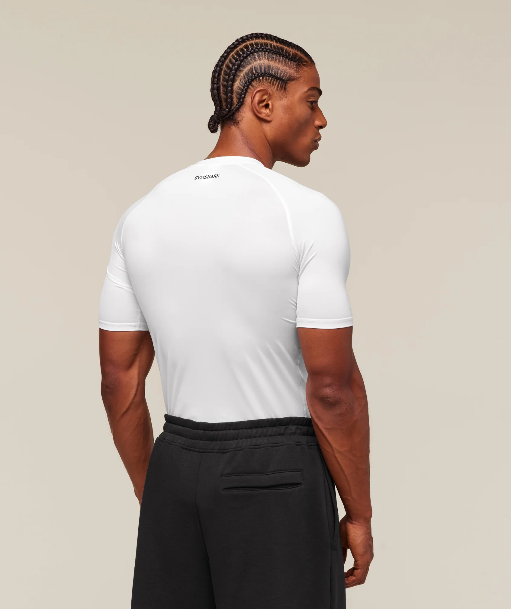 Person wearing a white t-shirt with a brand logo on the back, standing against a beige background.